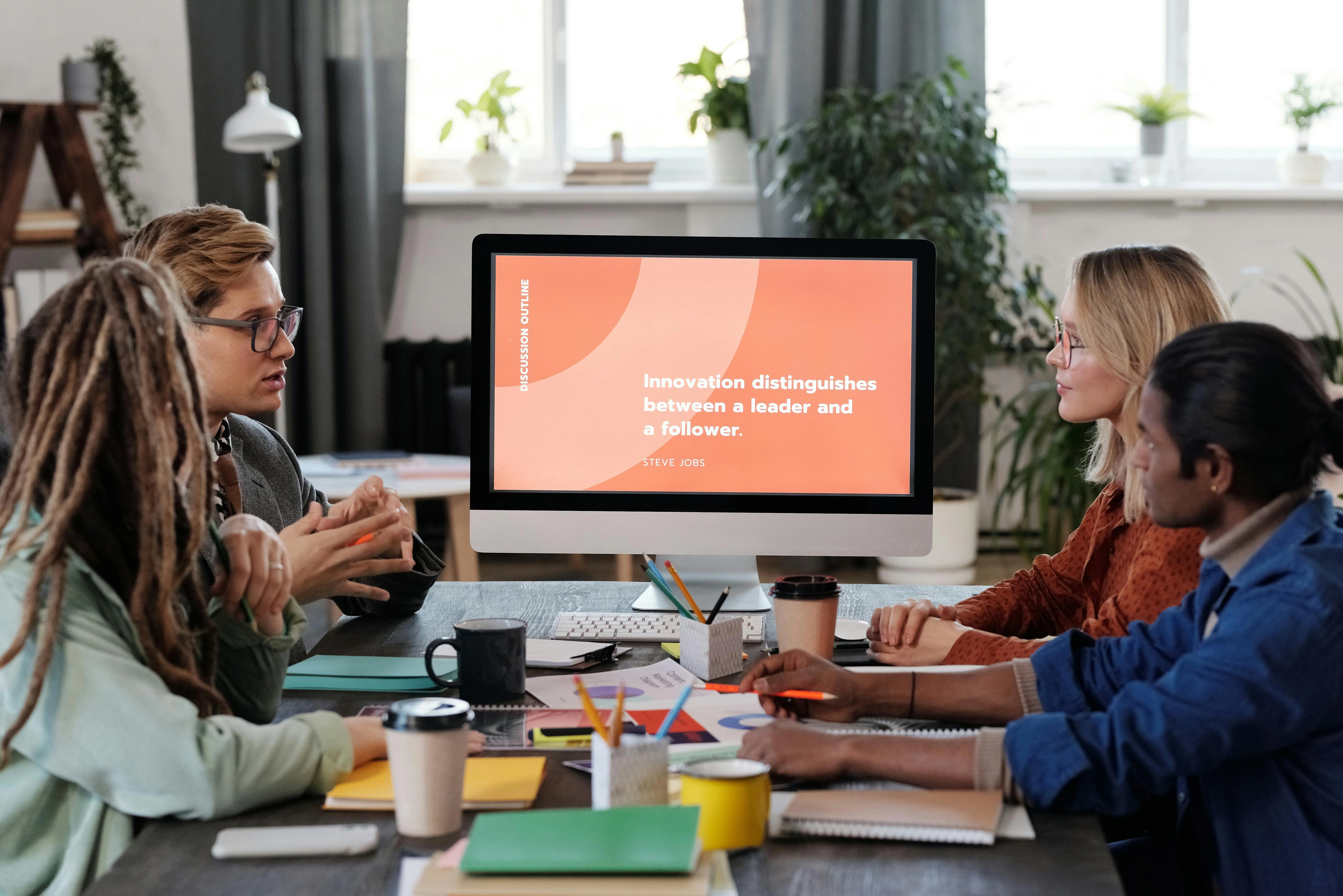 an image showing four employees sitting across a table with a desktop computer on the table depicting employee engagement